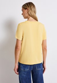 Korte mouwen gele top met een ronde hals, gladde textuur en hoogwaardige stof. Draag met blauwe denim jeans, wat een ontspannen pasvorm laat zien.
