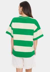 Grün-weiße gestreifte, übergroße T-Shirt mit kurzen Ärmeln und rundem Ausschnitt. Getragen über weißen Shorts mit Spitzenbesatz.