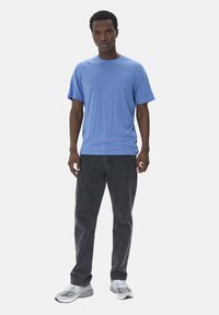 Blå kortärmad T-shirt i mjukt tyg, matchad med mörka jeans och grå sneakers. Rakt snitt och rund halsringning.