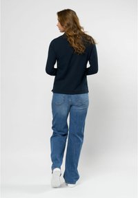 Mørkeblå langermet topp med tettsittende design, kombinert med lysblå vide jeans. Hvite joggesko fullfører antrekket.