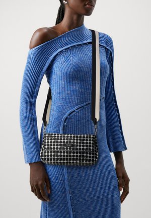 Black and white patterned crossbody bag with a rectangular shape, featuring a top flap and a contrasting strap on a blue ribbed dress.