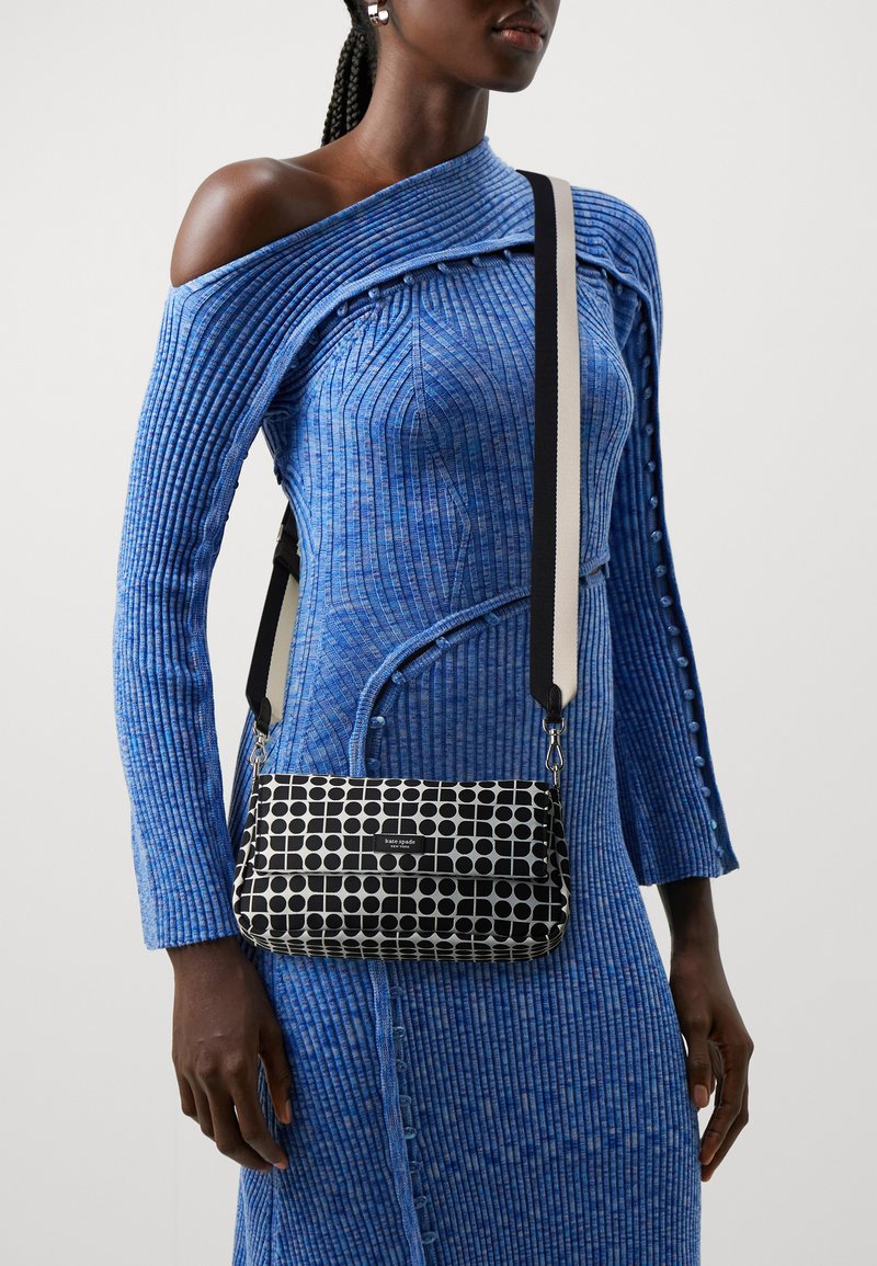 Borsa a tracolla in bianco e nero a fantasia con forma rettangolare, dotata di patta superiore e tracolla a contrasto su un vestito blu a coste.