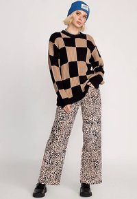 Maglione a coste nero e beige con motivo a quadri abbinato a pantaloni a gamba larga con stampa animalier beige e nera, completato da scarpe nere.