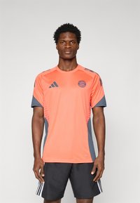 Oranje sportshirt met grijze accenten, met korte mouwen, ronde halslijn en een Bayern München-logo op de borst.