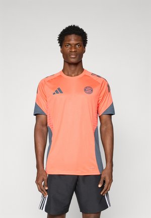 Orange sports shirt with gray accents, featuring short sleeves, round neckline, and a Bayern Munich logo on the chest.