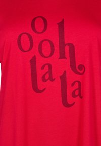 Červené bavlnené tričko s nápisom "ooh la la" v veľkej, tmavohnedej typografii s rôznymi veľkosťami a oblejšími akcentmi.