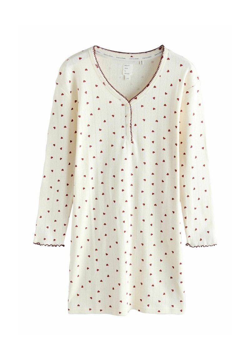 Kudotunnyt yö-tunika kermansävyssä, jossa on punaisia sydänkuvioita ja V-pääntie koristeompeleilla. Pitkät hihat, joissa on aaltoilevat reunat.