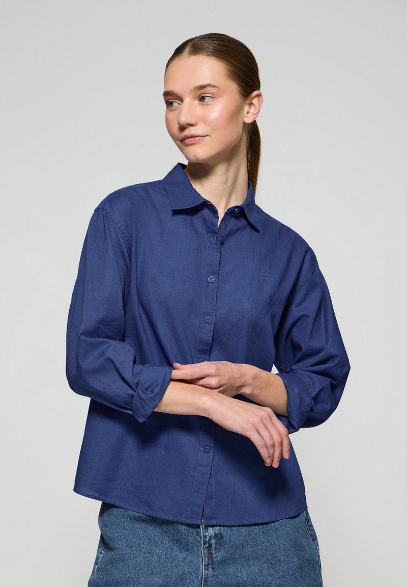 Mörkblå, långärmad skjorta med knappstängning, tillverkad av textil med struktur, med klassisk krage och uppvikta ärmar. Diskret logotypdetalj på bröstet.