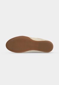 Semelle de chaussure avec grip en caoutchouc marron présentant de petites bosses circulaires sur l'avant-pied et le talon, bord supérieur beige visible sur fond blanc.
