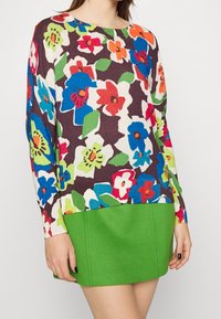 Wielokolorowy sweter z floralnymi wzorami na ciemnym tle, zestawiony z gładką zieloną spódnicą. Miękki dzianinowy materiał, długie rękawy.