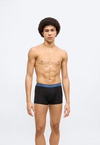 Μαύρα αντρικά σορτς μποξέρ με μπλε λωρίδα στη μέση που φέρει το λογότυπο «TOMMY HILFIGER». Το υλικό φαίνεται λείο και εφαρμοστό, με μικρό μήκος.