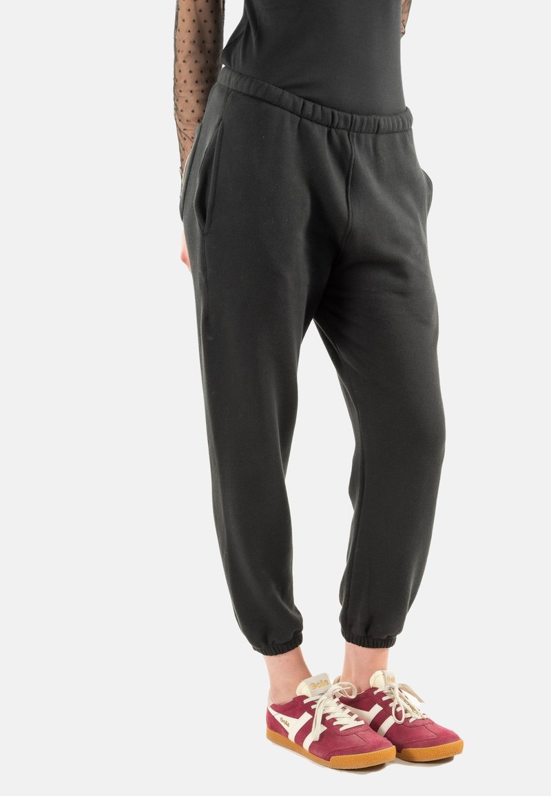Pantalones de chándal negros con cintura elástica, puños ajustados y bolsillos laterales, combinados con zapatillas rojas y blancas con suela de goma.