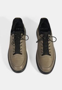 Baskets en cuir couleur taupe clair avec lacets et accents noirs. Présentent une forme de bout rond et une texture lisse. Logo "DESA" visible à l'intérieur.