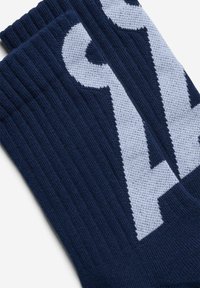 Dunkelblaue Strümpfe aus Strick mit geripptem Muster und großem weißem Grafikdesign. Akzentuiert durch kontrastierende Farben und einen bequemen Sitz.