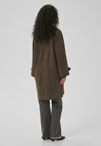 Brown suede long coat with bell sleeves and a back vent, paired with gray wide-leg jeans and black heeled shoes. Texture appears soft.