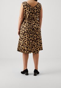 Vestido de estampado leopardo con espalda en V, diseño sin mangas, cintura ceñida y falda fluida. Combinado con zapatos de tacón cuadrado negros.