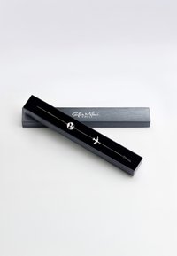 Silverarmband i en svart låda, med glob- och flygplansberlocker. Lådan har matt yta och vit textlogotyp på toppen.