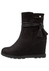 Stivale alla caviglia nero con tacco a cuneo, realizzato in suede, con una finitura liscia, passante in pelle avvolgente e dettaglio con nappina. Suola in gomma resistente.