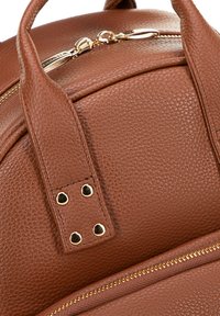 Sac à dos en cuir brun texturé avec quincaillerie dorée, deux poignées et une fermeture éclair avec une bordure d'accent le long du bord.