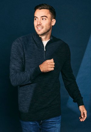Dark navy pullover sweatshirt with a quarter-zip collar, long sleeves, and a textured fabric, paired with blue jeans.