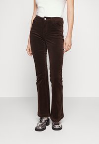 Bruna kordflorbyxor med utsvängda ben och framfickor, med en knappstängning och en mjuk yta. Bärs tillsammans med silverfärgade platåskor.