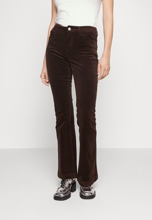 Pantalons évasés en velours côtelé marron avec poches avant, présentant une fermeture à bouton et une texture lisse. Portés avec des chaussures à plateforme argentées.