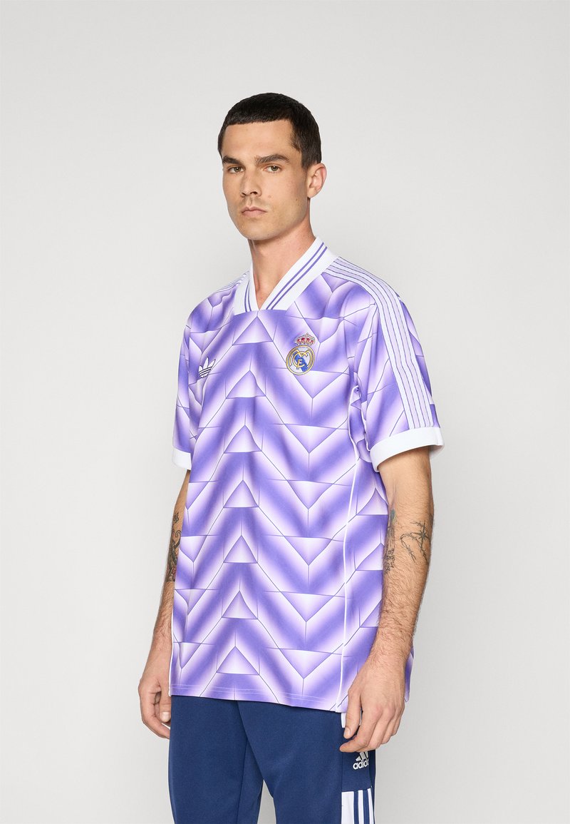 Camiseta de fútbol morada con un patrón geométrico, que presenta un cuello blanco, tres rayas blancas en las mangas y un logo del club en el pecho.