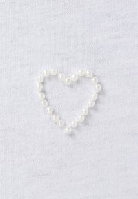 Witte stof achtergrond met een hartvorm gemaakt van kleine, ronde witte parels. De parels zijn gelijkmatig verdeeld en glanzend van uiterlijk.