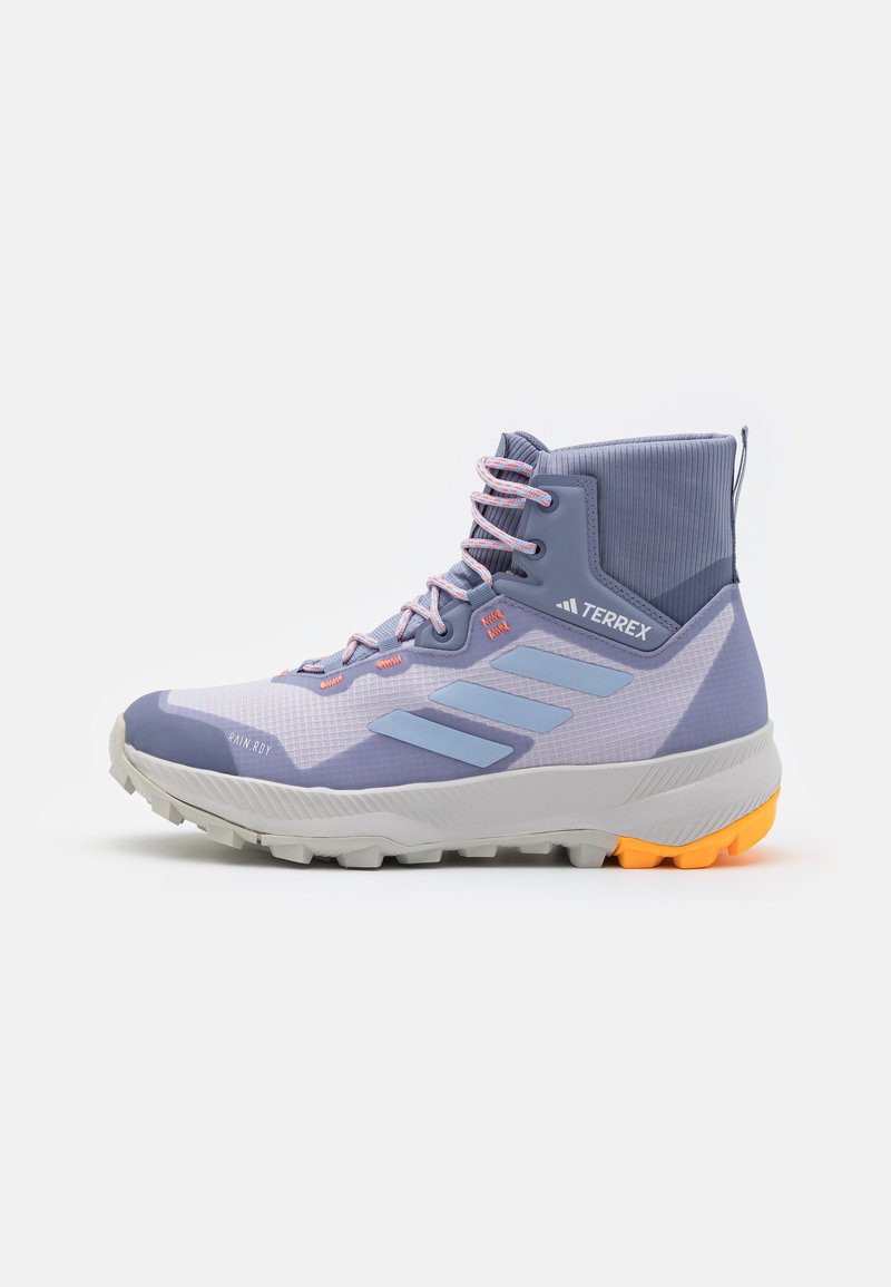 Wysokie buty outdoor z jasnofioletową siateczką, wzmocnionymi szarymi akcentami, różowymi sznurowadłami oraz teksturowaną szaro-pomarańczową podeszwą z pomarańczowym obcasem.