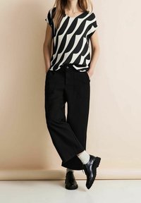 Top de manga corta en patrón de ondas en blanco y negro, combinado con pantalones negros de cintura alta y zapatos negros de cordones con calcetines blancos.