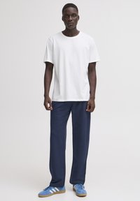 Vit bomullst-shirt med korta ärmar; kombinerad med marinblå sweatpants; blå sneakers med tre vita ränder på sidan.