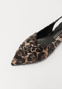 Chaussure slingback à bout pointu avec un imprimé léopard, présentant un détail noué sur le devant et une texture satinée lisse.