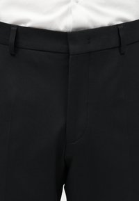 Μαύρο επίσημο παντελόνι με θηλιές για ζώνη, φορεμένο με λευκό πουκάμισο, με έμφαση στη μέση και την περιοχή του επάνω μηρού.