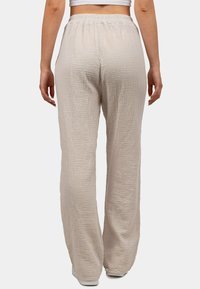 Lichtbeige, gestructureerde wijde broek met een zachte, gekreukte stof, voorzien van een elastische tailleband en een relaxte pasvorm.