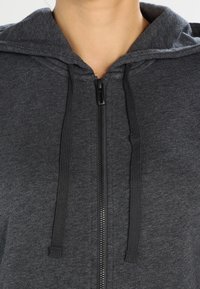 Szara bluza z kapturem na zamek błyskawiczny, o miękkiej teksturze, ze sznurkami i dużym kapturem. Posiada zamek błyskawiczny na całej długości oraz prosty design.