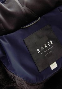 Námornícky modrá vnútorná tkanina s textúrovanou čiernou etiketou, na ktorej je napísané "BAKER by TED BAKER LONDON." Mäkký, nadýchaný akcent pozdĺž okraja.