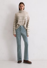 Beige gestreepte trui met een hoge kraag, gecombineerd met lichtgroene corduroy broek met patchzakken en bruine schoenen.