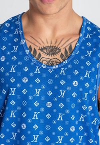 Modrá tielko bez rukávov s bielymi logami, s okrúhlym výstrihom. Mäkkučký textil s hladkým povrchom.