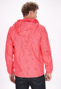 Svetložltý ľahký kabát s kapucňou, ktorý má abstraktný líniový vzor. Elastické manžety a lem, hladká textúra. Zobrazený pohľad zozadu.