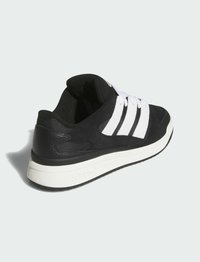 Zapatilla deportiva negra con tres rayas blancas, materiales de ante y cuero, cuello acolchado y suela de goma texturizada. Acentuada con una entresuela blanca.