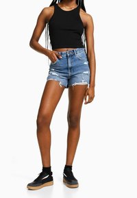 Svart ribbad kort topp kombinerad med slitna denimshorts med fransiga kanter och hög midja. Skor är svarta sneakers med gummisulor.