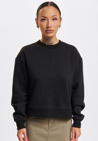 Svart cropped sweatshirt i et mykt materiale med rund hals og senket skuldre. Har ribbede mansjetter og kant for en komfortabel passform.