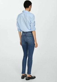 Chemise boutonnée à rayures bleues et blanches, manches retroussées, associée à un jean skinny bleu foncé. Le tissu semble lisse avec un aspect denim classique.