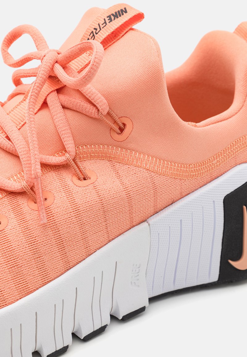 Zapatillas Nike Free en coral con tejido texturizado, que presentan un sistema de cordones curvados, acentos naranjas prominentes y un diseño de suela en blanco y negro.