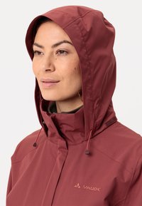 Giacca impermeabile bordeaux con chiusura a zip e cappuccio regolabile. Tessuto testurizzato e logo sul lato sinistro del petto. Presenta dettagli con cordoncino.