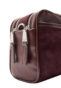 Burgundowa torebka ze skóry i zamszu z srebrnymi zamkami błyskawicznymi, wyróżniającym się pierścieniowym akcentem oraz kontrastowym przeszyciem. Kompaktowy, prostokątny kształt.