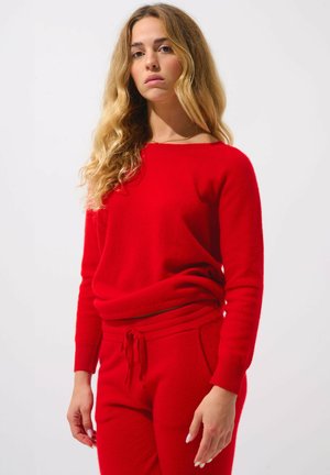 Czerwony sweter dziany z okrągłym dekoltem i długimi rękawami, połączony z czerwonymi dopasowanymi spodniami z troczkiem w pasie i kieszeniami po bokach.
