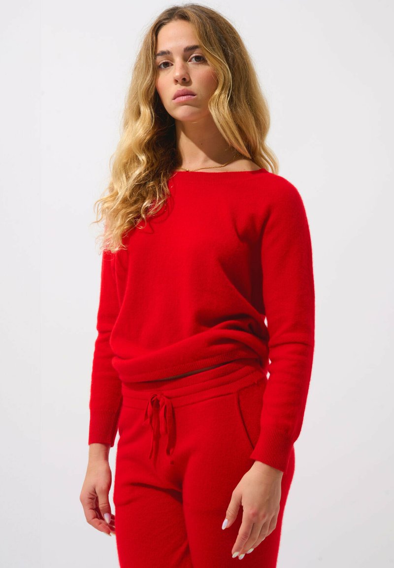 Roter Strickpullover mit Rundhalsausschnitt und langen Ärmeln, kombiniert mit roten engen Hosen mit einem Kordelzugbund und Seitentaschen.