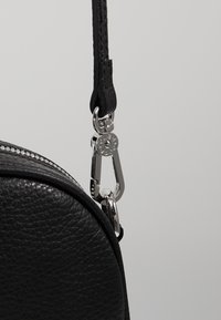 Borsa nera in pelle con superficie testurizzata, dotata di un gancio metallici argentato a moschettone e un dettaglio della tracolla. Chiusura con zip nella parte superiore.