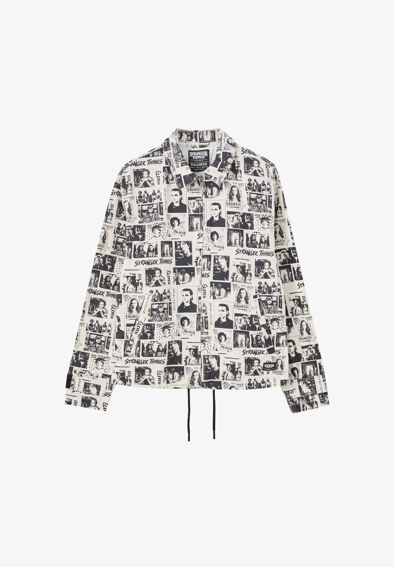 Chaqueta de color negro y blanco con cuello que presenta diversas imágenes impresas y texto de "Stranger Things", con un dobladillo ajustable y mangas largas.